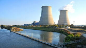 a nuclear power plant with two concrete smoke stacks stands beside a body of water